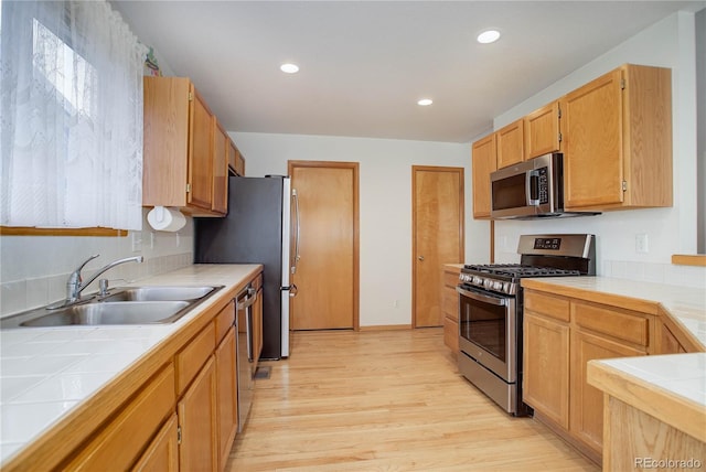 kitchen featuring light brown cabinets, appliances with stainless steel finishes, sink, light wood-type flooring, and tile counters