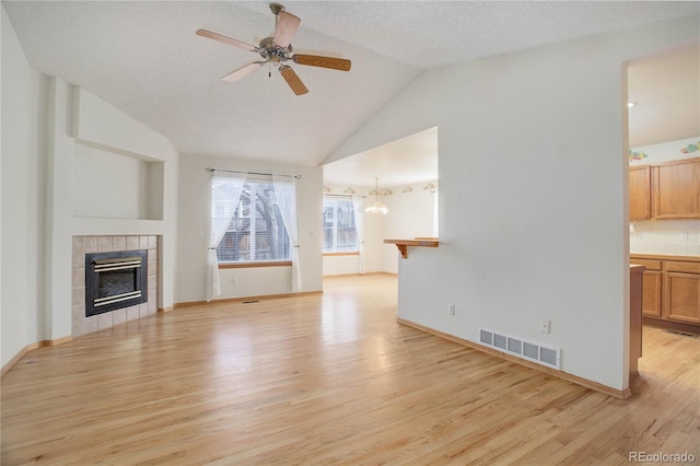 unfurnished living room with a fireplace, a textured ceiling, light hardwood / wood-style flooring, vaulted ceiling, and ceiling fan with notable chandelier