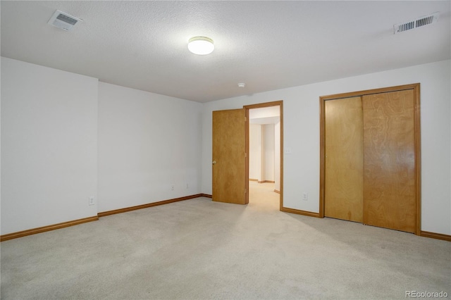 unfurnished bedroom featuring a closet, a textured ceiling, and light carpet