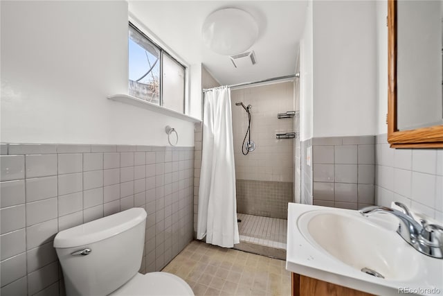 bathroom with visible vents, tile walls, wainscoting, toilet, and tiled shower