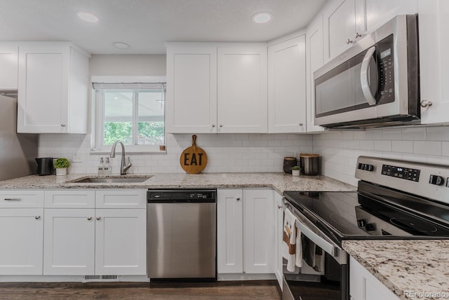 6059 Routt St, Arvada, CO 80004 - kitchen with appliances with stainless steel finishes, white cabinetry, dark wood finished floors, decorative backsplash, and light stone counters
