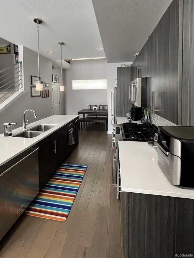 kitchen featuring appliances with stainless steel finishes, dark hardwood / wood-style floors, pendant lighting, sink, and a textured ceiling