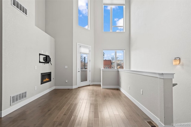 unfurnished living room featuring a glass covered fireplace, dark wood-style flooring, and visible vents