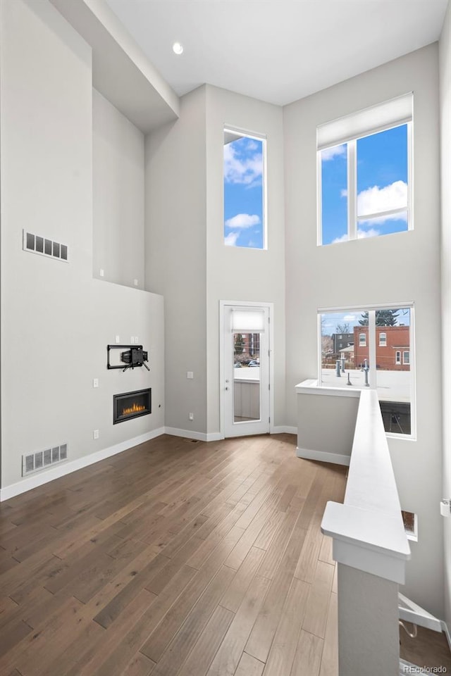 living room with light wood-style flooring, visible vents, baseboards, and a glass covered fireplace