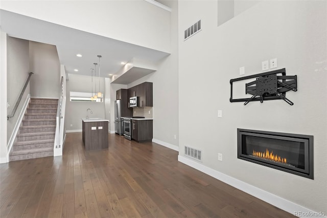 unfurnished living room featuring dark wood-style floors, stairs, a sink, and visible vents