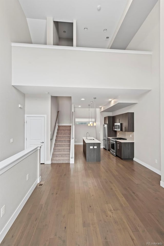 unfurnished living room with dark wood-style flooring, stairway, a towering ceiling, a sink, and baseboards