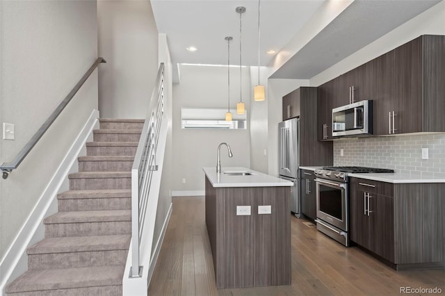 kitchen with dark wood-style floors, decorative backsplash, a kitchen island with sink, a sink, and high quality appliances