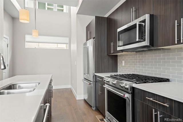 kitchen with high end appliances, dark wood-type flooring, a sink, light countertops, and backsplash