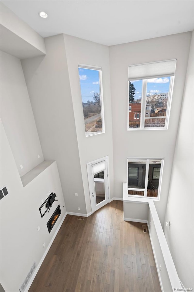 unfurnished living room featuring a warm lit fireplace, visible vents, baseboards, wood finished floors, and recessed lighting