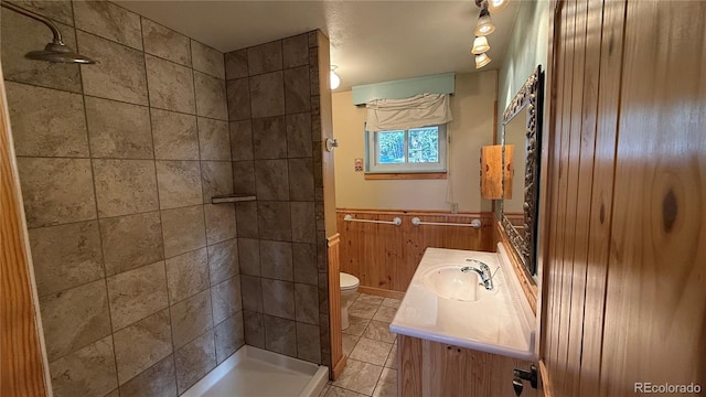 bathroom featuring vanity, wood walls, tile patterned flooring, toilet, and tiled shower