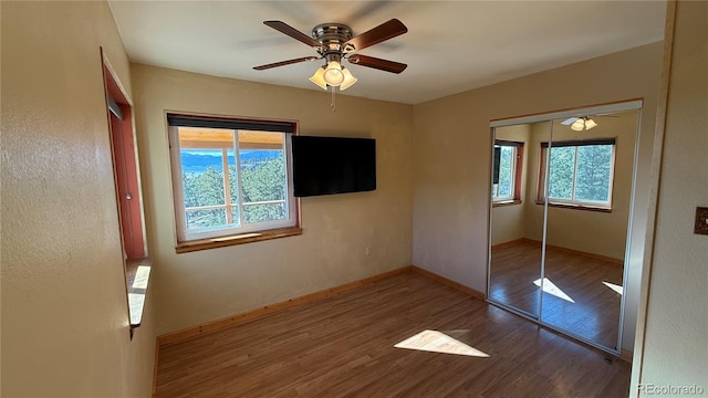 unfurnished bedroom with wood-type flooring, a closet, multiple windows, and ceiling fan