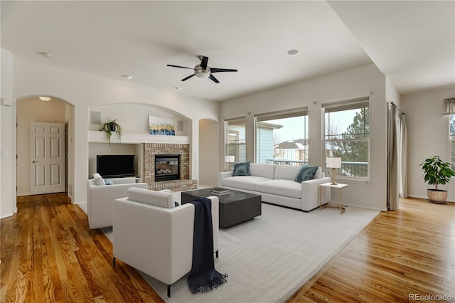 living room featuring a brick fireplace, hardwood / wood-style flooring, and ceiling fan