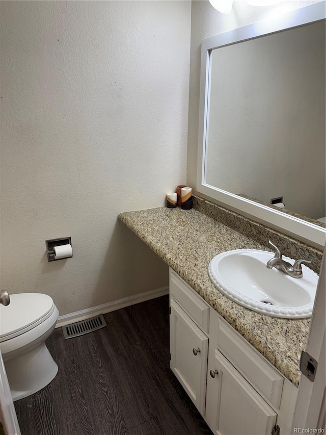 bathroom with visible vents, toilet, vanity, wood finished floors, and baseboards