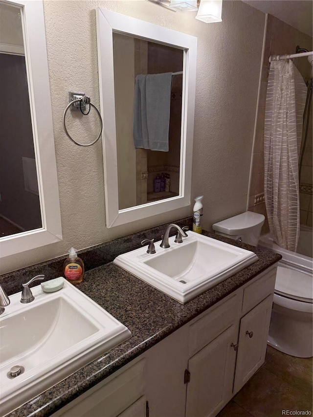 full bath with a textured wall, a sink, toilet, and double vanity