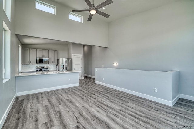 unfurnished living room featuring ceiling fan, light hardwood / wood-style floors, and a high ceiling