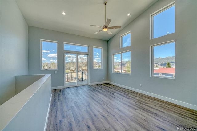 empty room with a mountain view, ceiling fan, a towering ceiling, and light hardwood / wood-style flooring