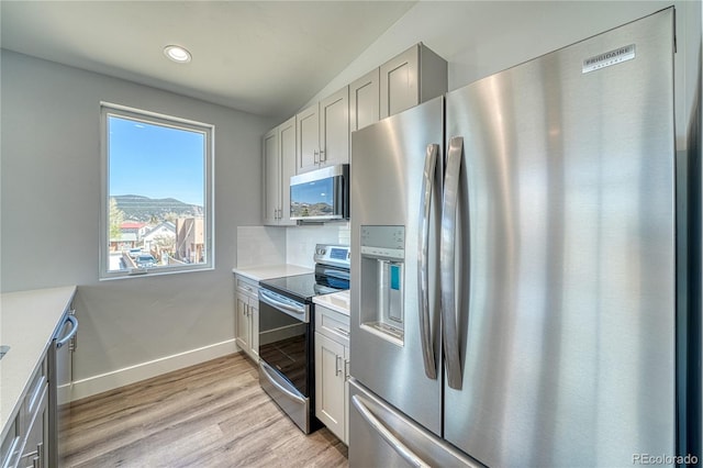 kitchen with gray cabinetry, tasteful backsplash, vaulted ceiling, appliances with stainless steel finishes, and light wood-type flooring