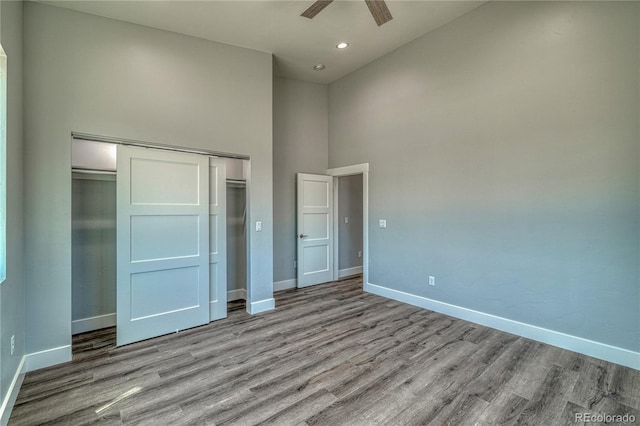 unfurnished bedroom featuring ceiling fan, a closet, a towering ceiling, and light hardwood / wood-style flooring