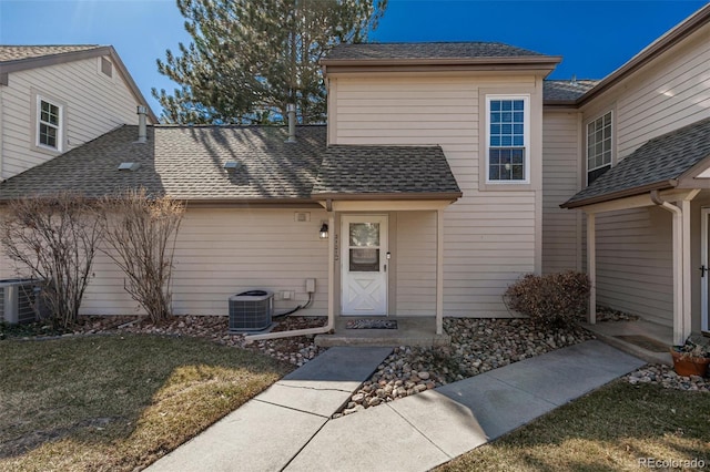 view of front of house with a shingled roof, central AC unit, and a front lawn