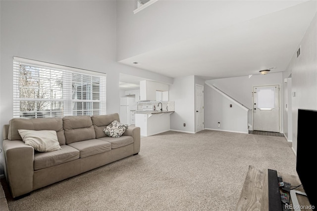 living area featuring light colored carpet, visible vents, a high ceiling, and baseboards