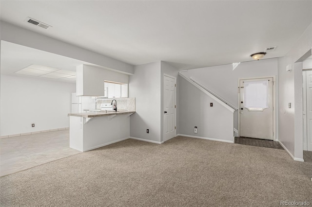 unfurnished living room featuring light colored carpet, visible vents, a sink, and baseboards