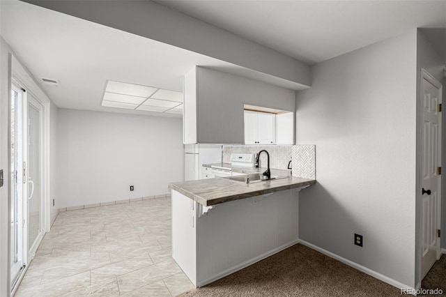 kitchen with visible vents, decorative backsplash, a breakfast bar area, a peninsula, and a sink