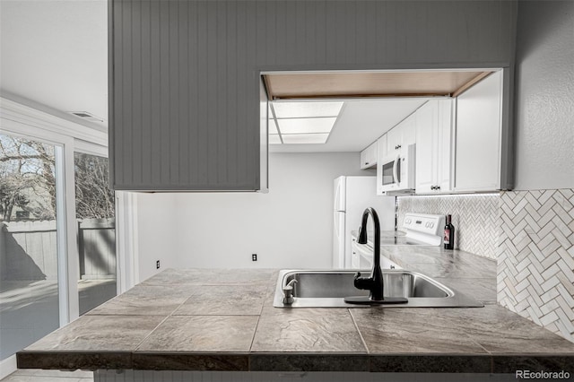 kitchen featuring white microwave, a peninsula, range with electric cooktop, a sink, and tasteful backsplash