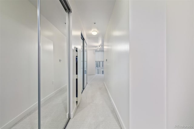 hall with light colored carpet, attic access, and baseboards