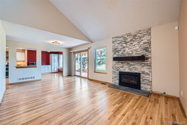 unfurnished living room featuring a stone fireplace, wood finished floors, visible vents, and a textured ceiling