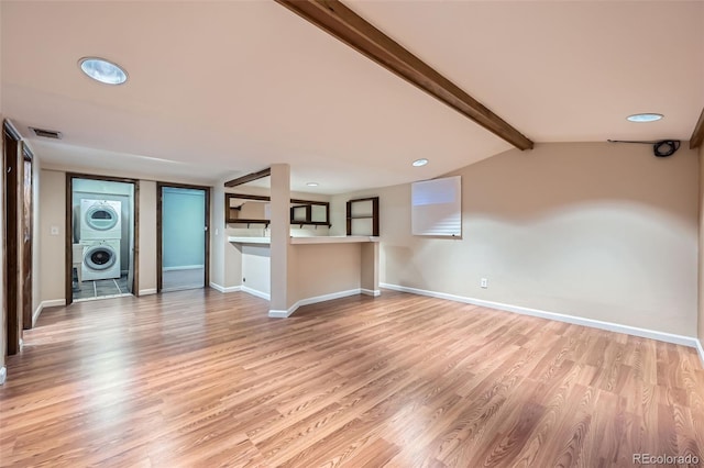 unfurnished living room featuring baseboards, visible vents, lofted ceiling with beams, stacked washer and dryer, and light wood-type flooring