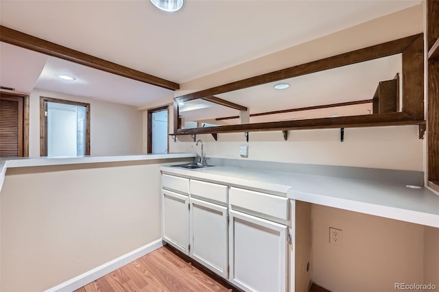 kitchen with a sink, light countertops, white cabinetry, beamed ceiling, and light wood-type flooring