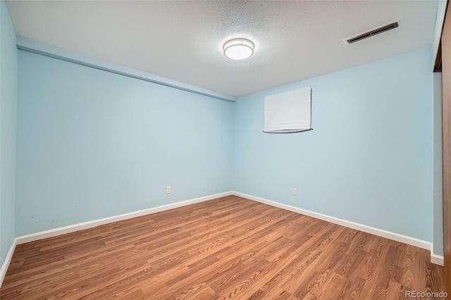 unfurnished room featuring visible vents, baseboards, a textured ceiling, and wood finished floors