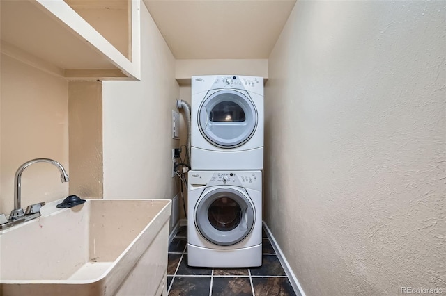 laundry area featuring dark tile patterned flooring, a sink, stacked washer / drying machine, laundry area, and a textured wall