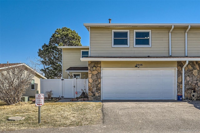 view of front facade with driveway, a gate, stone siding, fence, and a garage