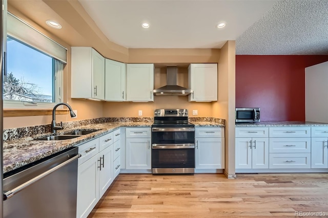 kitchen featuring a sink, stone countertops, light wood-style floors, appliances with stainless steel finishes, and wall chimney range hood