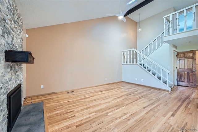 unfurnished living room with a stone fireplace, stairs, baseboards, and wood finished floors