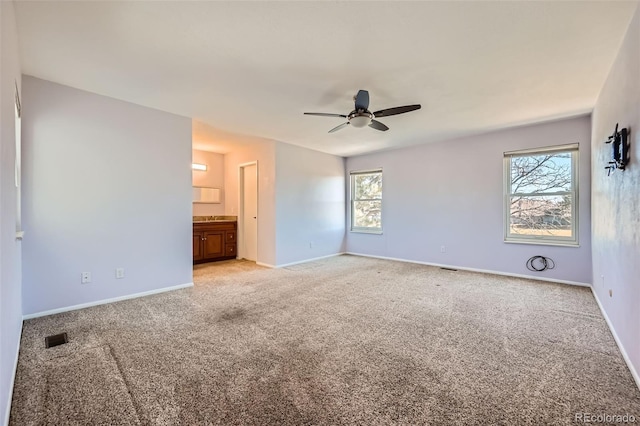 unfurnished bedroom with visible vents, connected bathroom, baseboards, ceiling fan, and light colored carpet