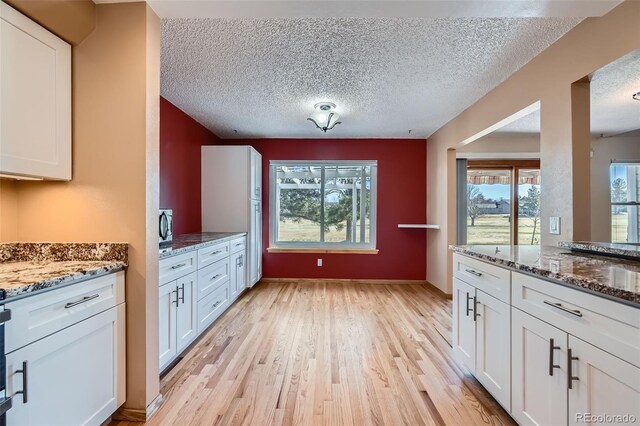 2446 S Vaughn Way Unit A, Aurora, CO 80014 - kitchen featuring dark stone countertops, white cabinets, light wood-style floors, and a textured ceiling