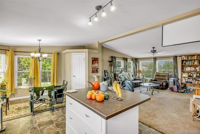 kitchen featuring a kitchen island, ceiling fan with notable chandelier, decorative light fixtures, white cabinetry, and lofted ceiling