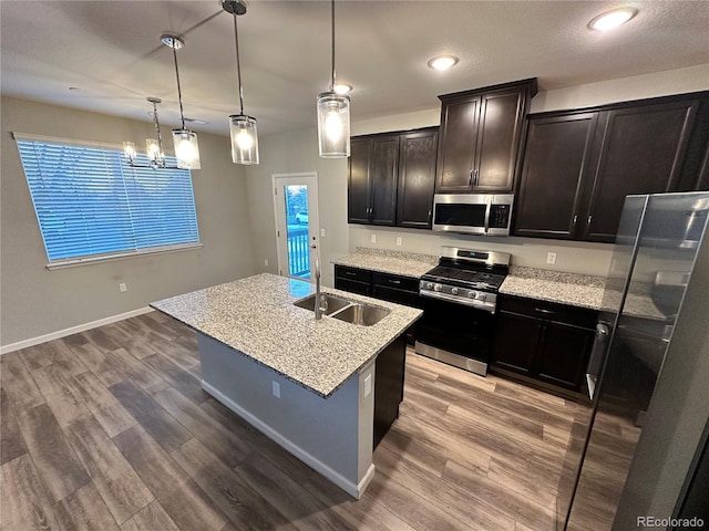 kitchen with pendant lighting, sink, stainless steel appliances, wood-type flooring, and an island with sink