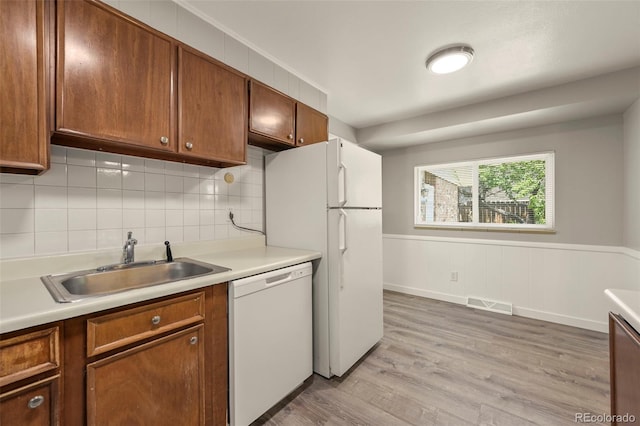 6432 Zephyr St, Arvada, CO 80004 - kitchen featuring white appliances, a sink, brown cabinets, light countertops, and a wainscoted wall