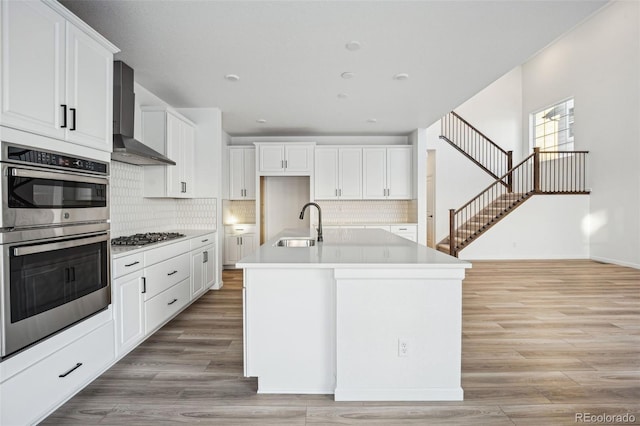 kitchen featuring wall chimney exhaust hood, sink, white cabinetry, a center island with sink, and stainless steel appliances