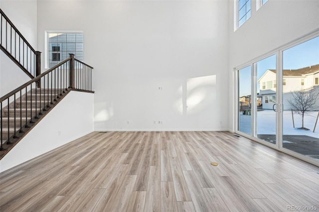 unfurnished living room featuring a towering ceiling and light hardwood / wood-style floors