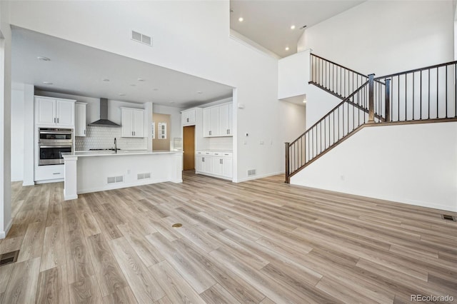 unfurnished living room featuring sink, light hardwood / wood-style floors, and a high ceiling