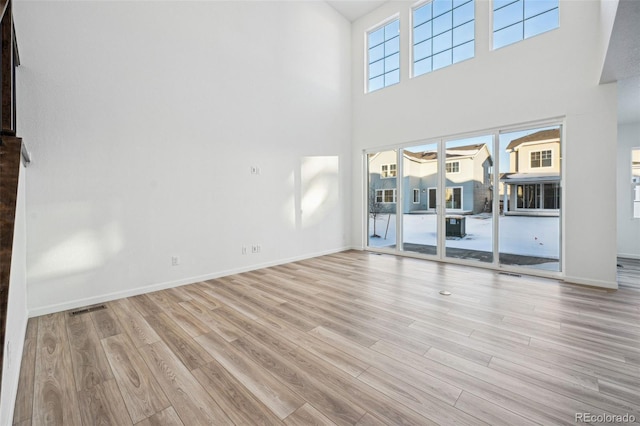 unfurnished living room featuring a high ceiling, plenty of natural light, and light wood-type flooring