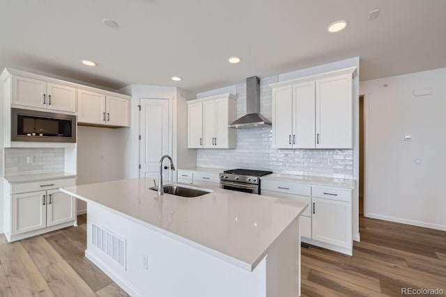 kitchen featuring wall chimney exhaust hood, gas stove, sink, and an island with sink