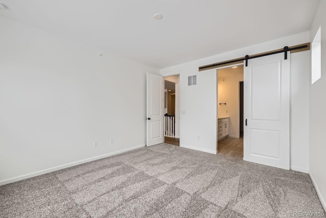 unfurnished bedroom featuring light carpet, a barn door, and ensuite bath