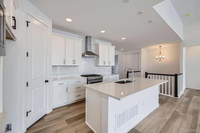 kitchen with white cabinets, wall chimney range hood, sink, light hardwood / wood-style flooring, and stainless steel gas stove