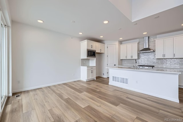 kitchen featuring stainless steel microwave, wall chimney range hood, tasteful backsplash, white cabinets, and light wood-type flooring