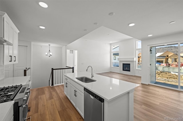 kitchen with appliances with stainless steel finishes, white cabinetry, sink, a kitchen island with sink, and light wood-type flooring